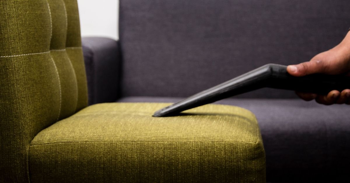 Close-up of a person vacuuming a patterned cushion on a dark fabric sofa indoors