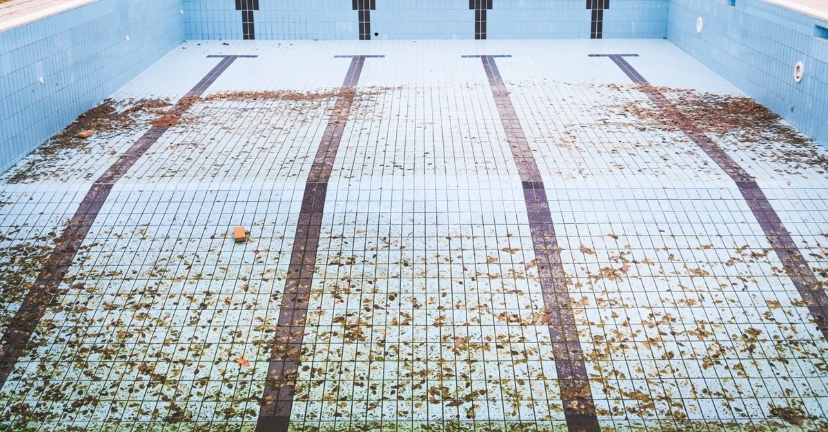 High-angle view of an empty in-ground swimming pool with leaves and debris on the floor