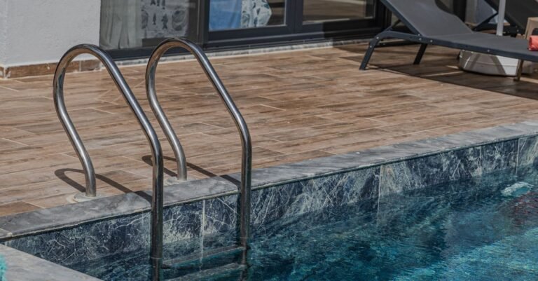Landscaped swimming pool with pale marble coping, timber decking and loungers in afternoon sun