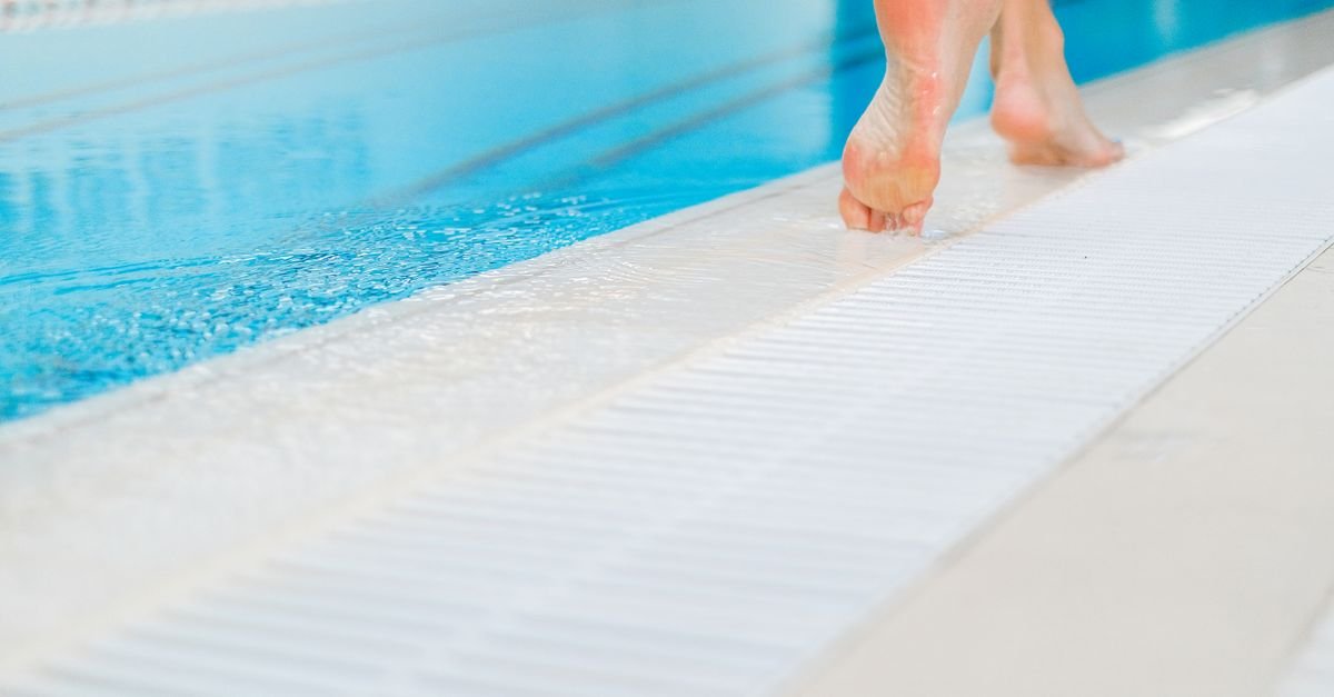 Bare feet walking along the wet tiled edge of a swimming pool