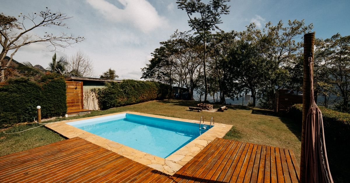 Outdoor swimming pool surrounded by dense greenery with timber decking running to the water's edge