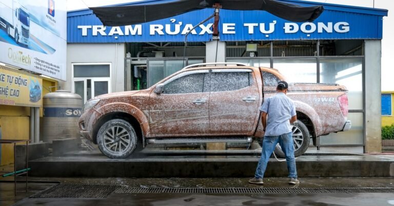 A worker cleaning a pickup truck with a pressure washer at an outdoor vehicle wash bay