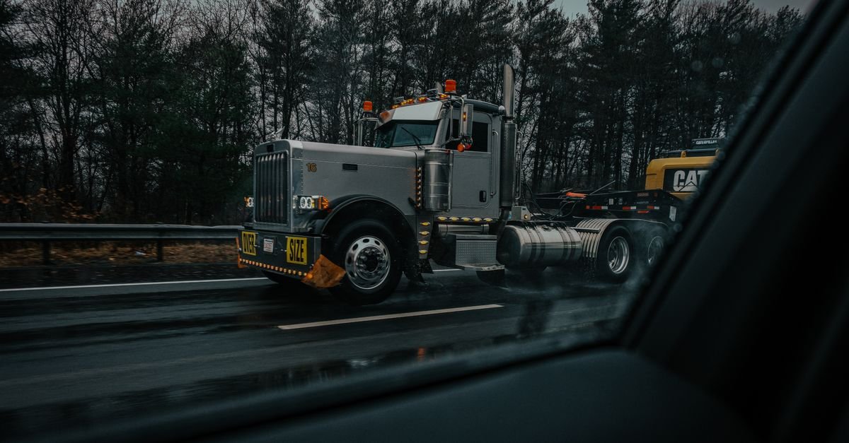 A large truck on a wet highway seen through road spray, the conditions that deposit road film