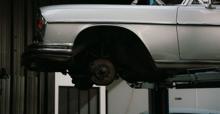 A classic car raised on a two-post workshop lift with its undercarriage, exhaust and suspension fully exposed