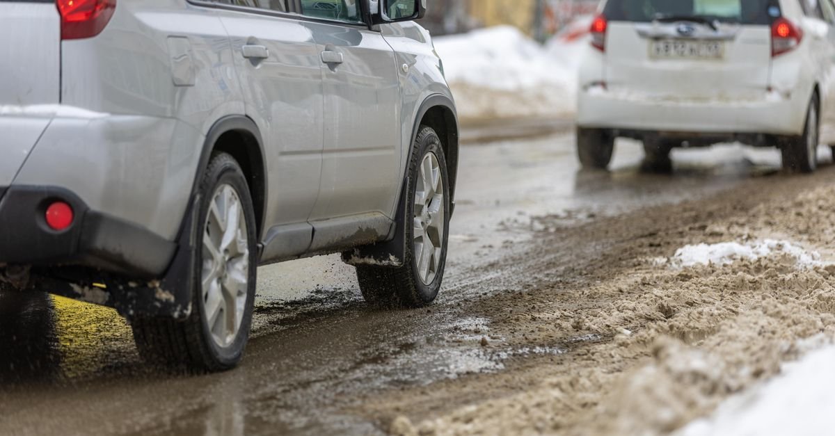 Two cars driving through grey slush on a snow-covered road during winter