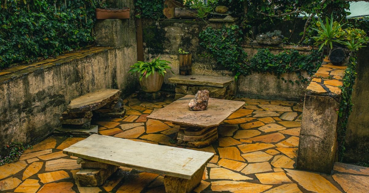 Stone garden patio with ivy-covered walls, stone benches and pale jointed paving