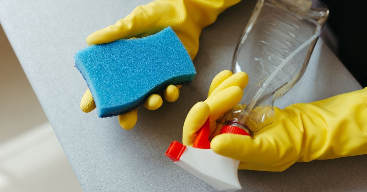 Gloved hands holding a sponge and a spray bottle ready to apply a cleaning solution