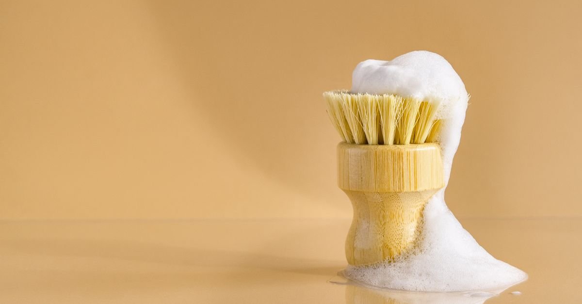 Cleaning brush covered in thick white foam against a plain beige background