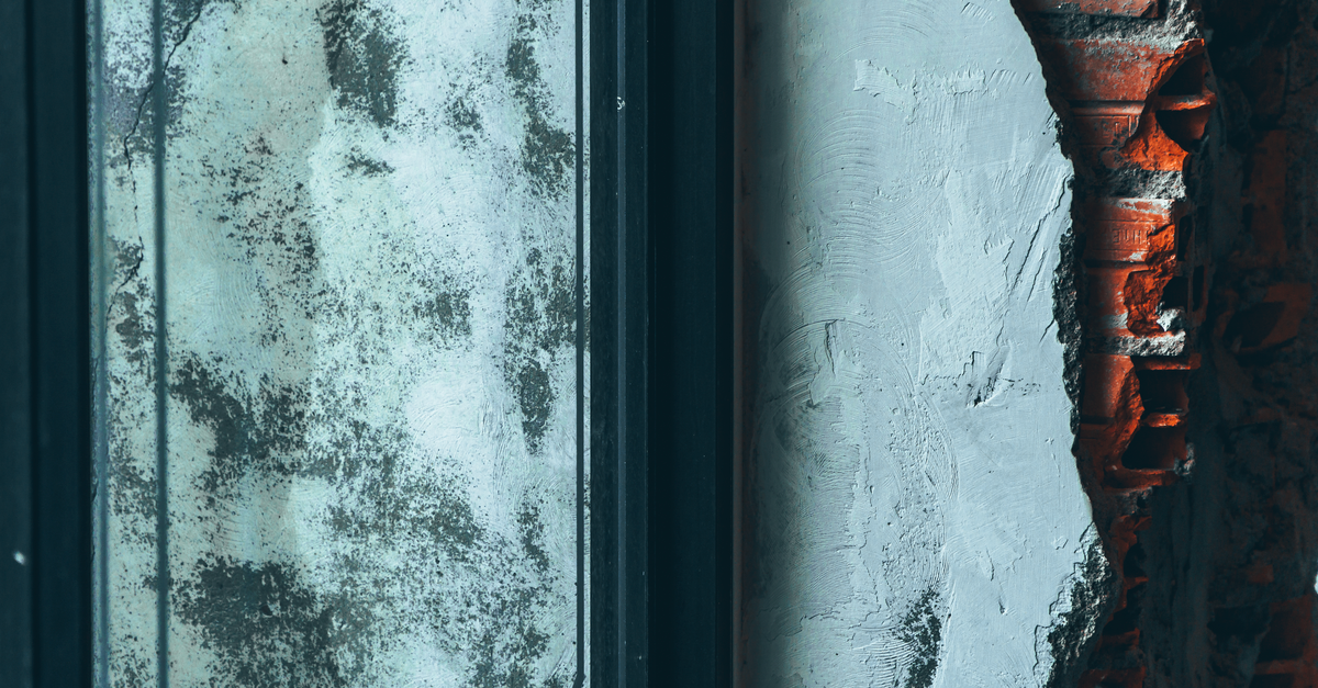 Close-up of a wall where the plaster render has come away to reveal the red brick underneath