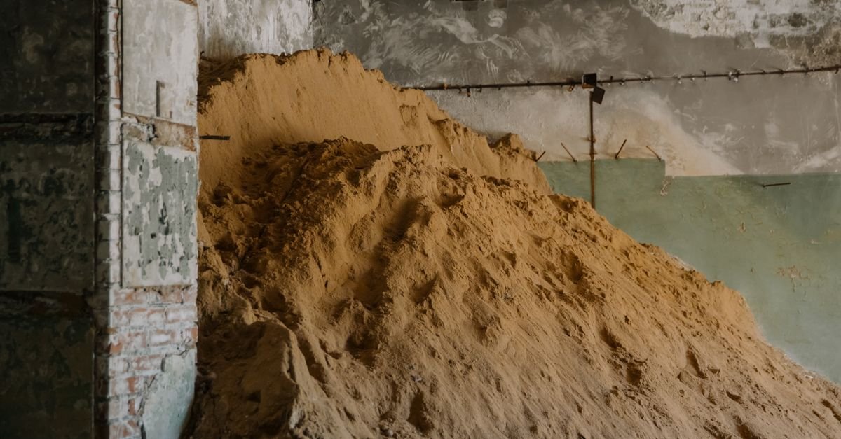 A large pile of loose sand stored inside an aged industrial building