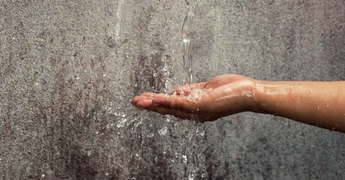 A hand catching a stream of water in front of a textured exterior wall