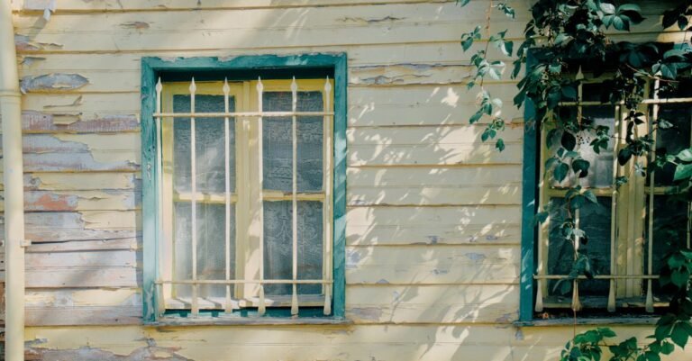 A weathered timber house facade with aged paint and climbing vines lit by low direct sunlight