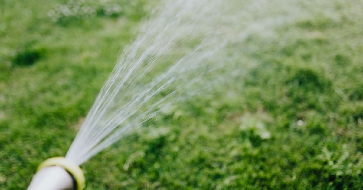 Wide spray of water from a hose nozzle over a lawn, illustrating flow volume rather than pressure