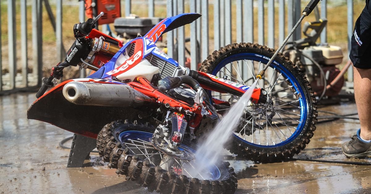 A motocross bike being rinsed with a pressure washer outdoors