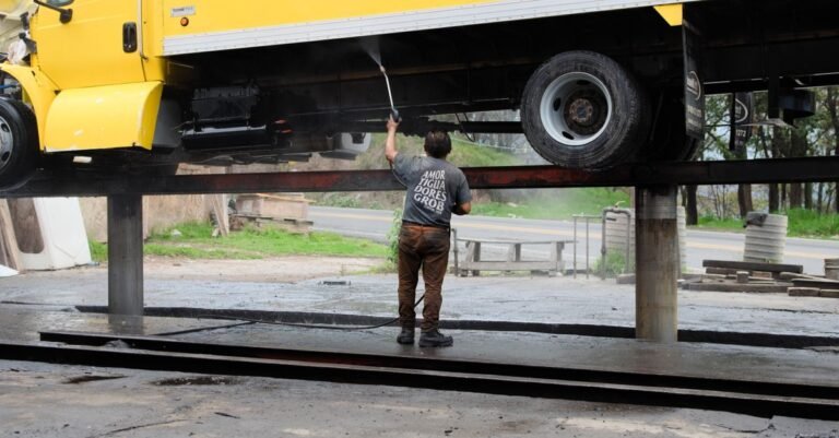 Worker power washing the underside of a raised truck at an outdoor service bay