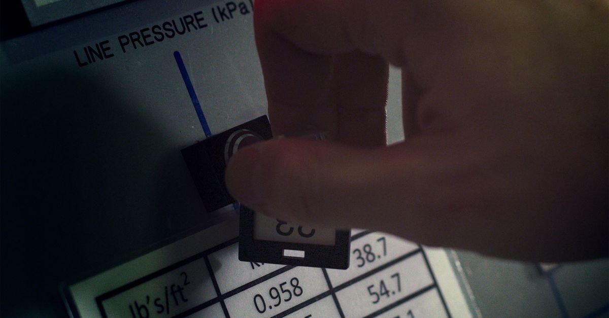 Close-up of a hand adjusting a pressure gauge dial on industrial equipment