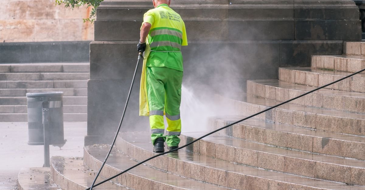 Worker in high-visibility gear pressure washing stone steps, wearing recommended safety equipment