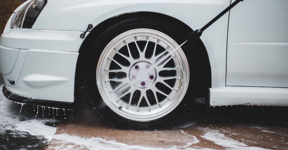 Pressure washer wand rinsing soap from a car wheel at a safe working distance