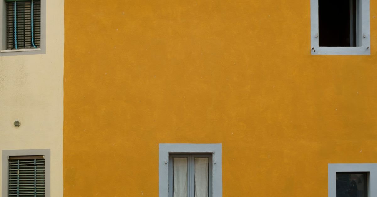 Painted stucco building facade in yellow and cream tones with window trim