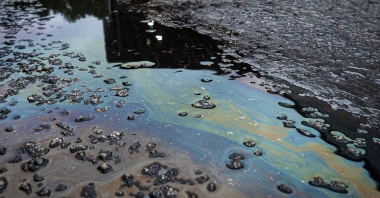 Iridescent oil spill spreading across a rough pavement surface