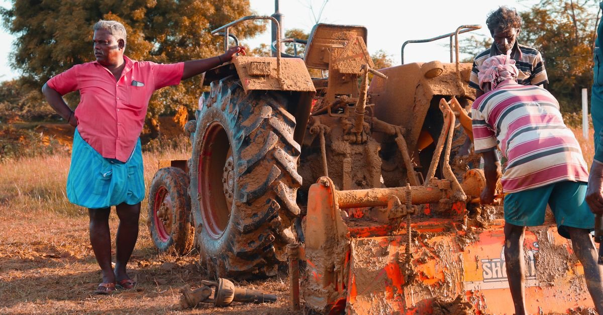 Men working on a mud-covered tractor in a rural field