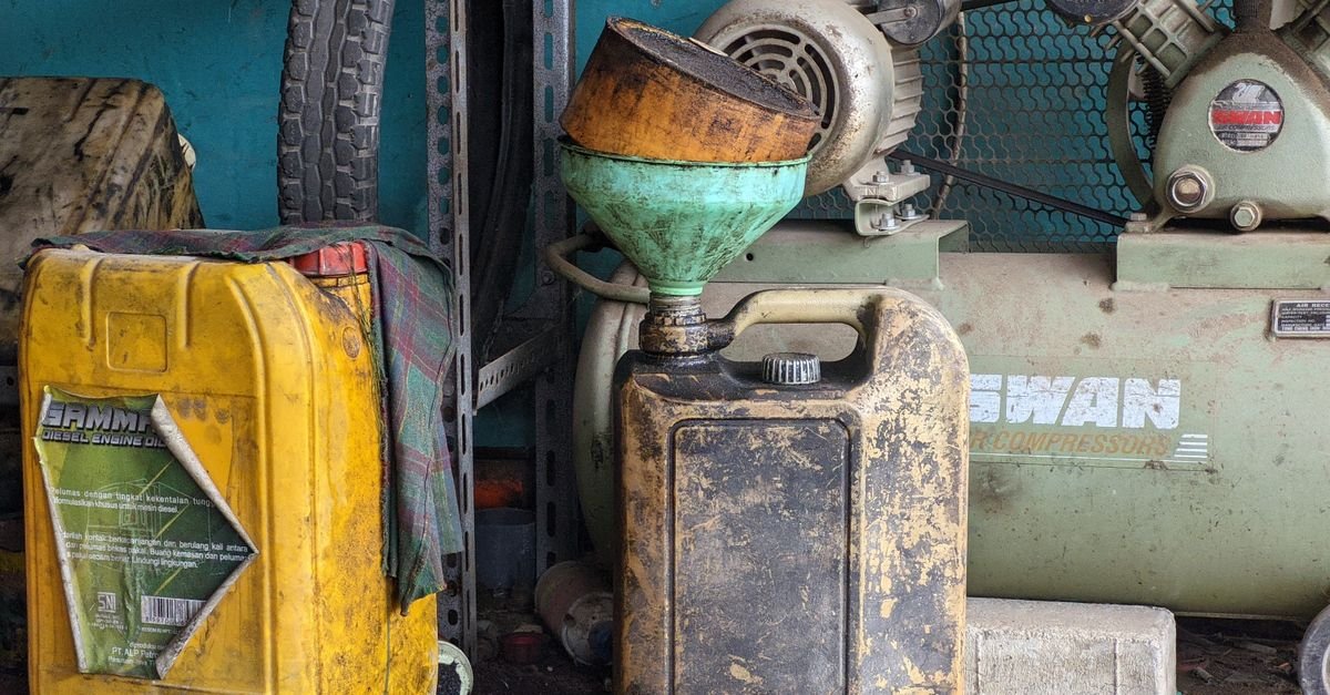 A worn metal drum and an old compressor standing in a dusty industrial workshop