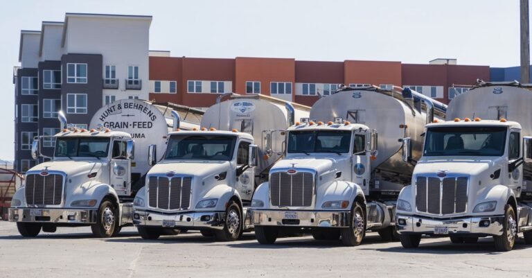 Four semi-trailers parked in an industrial yard beside grain silos, the fleet and agricultural work a high-flow pressure washer is bought for
