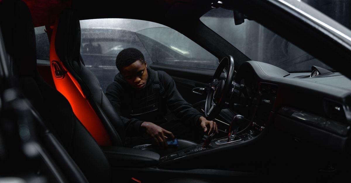 A man cleaning the inside of a car at night with a detailing tool and a torch