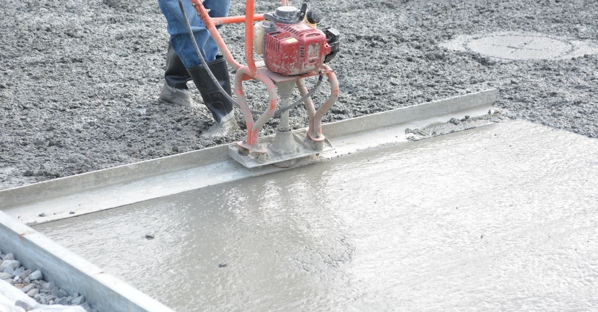 A construction worker running a power trowel across freshly poured concrete, the dense finish that stretches a gallon furthest