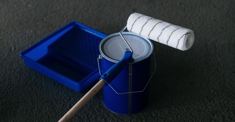 A sealer pail, roller and tray standing ready on a textured concrete floor before the first coat