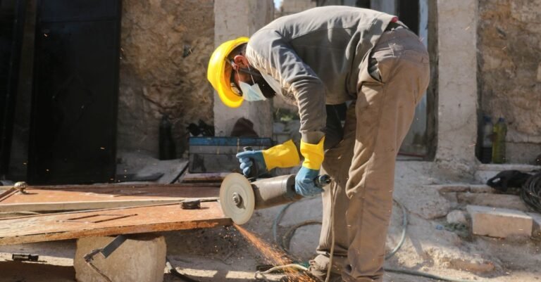 Man in protective gear running an angle grinder against a hard surface outdoors