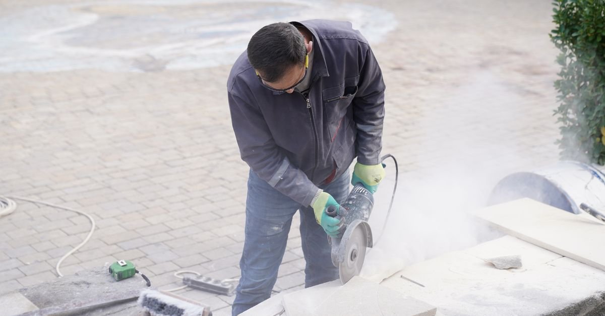 A construction worker running a power saw into stone outdoors, throwing visible dust
