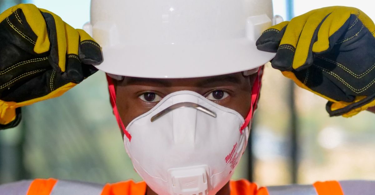 Close-up of a construction worker in a hard hat, gloves and an N95 mask