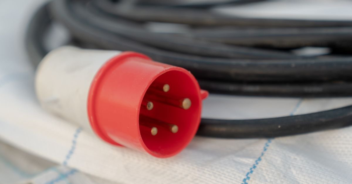 A red industrial electrical cable plug with its pins exposed, the connector standard being the first thing a cord has to match