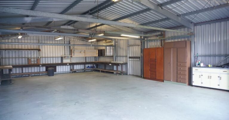 Empty garage bay with bare concrete floor, steel walls, storage cabinets and a workbench