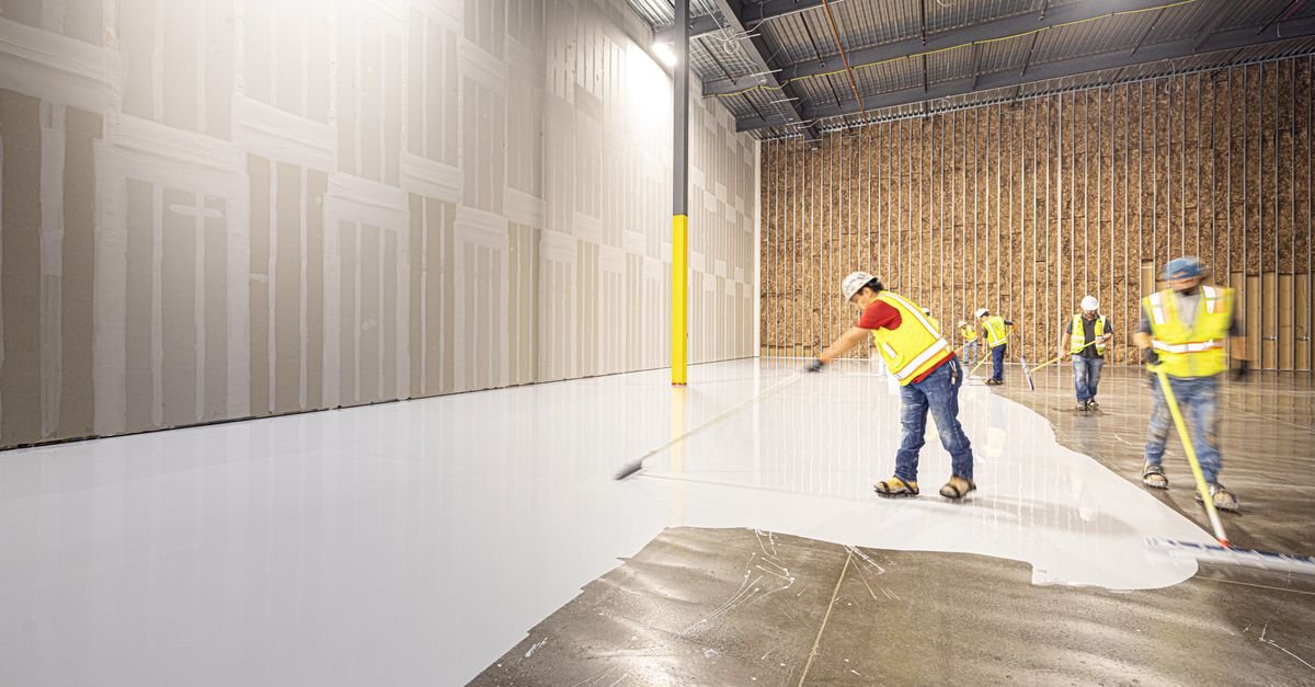Construction workers in hard hats placing and levelling a freshly poured concrete floor inside a building