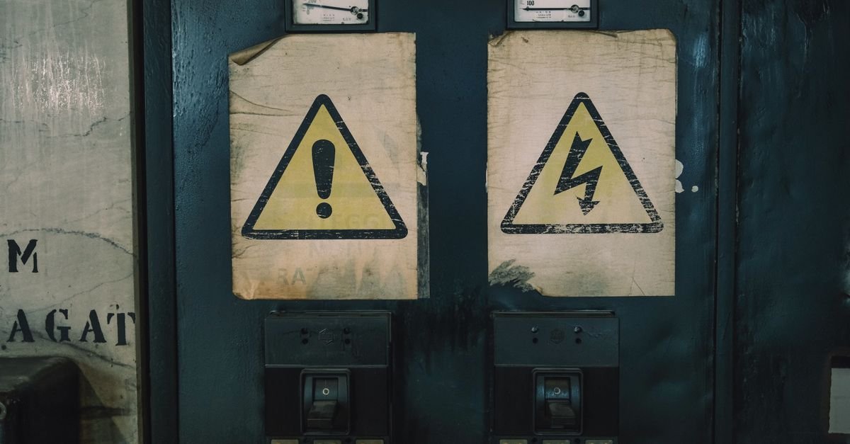 Two moulded-case protective devices mounted below ammeters on an aged electrical panel, under hazard labels