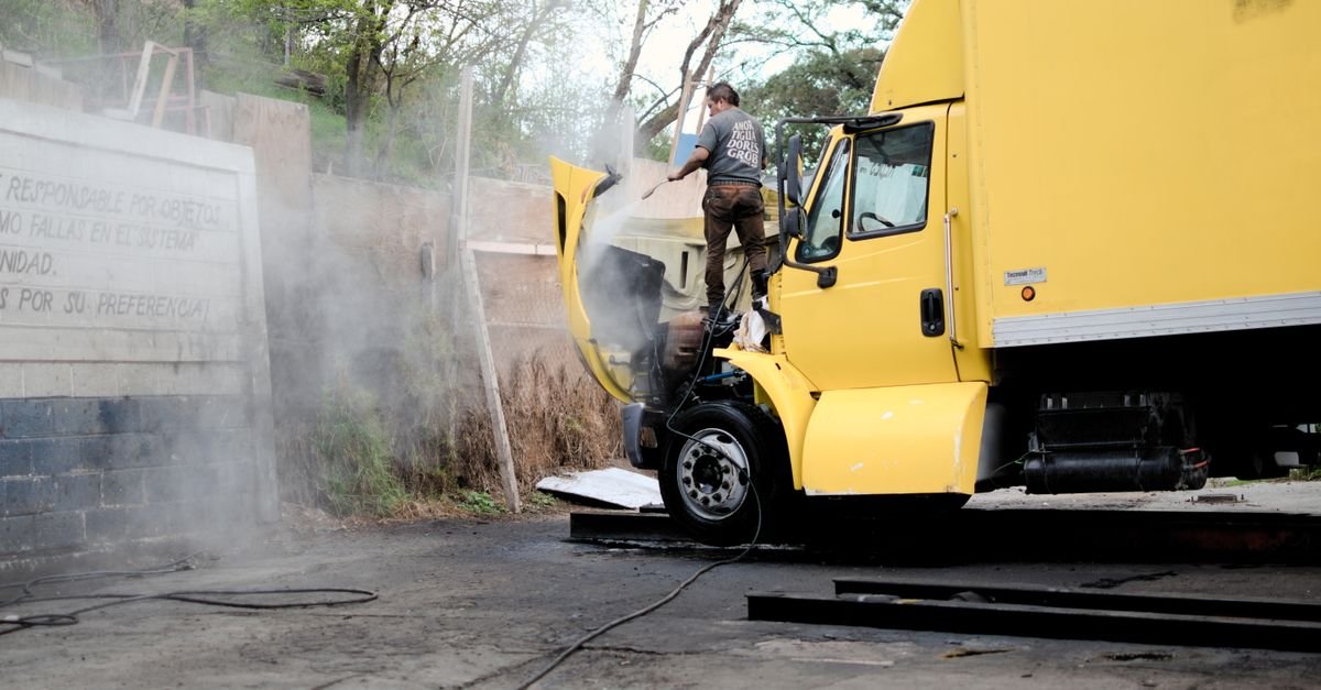 A mechanic working on the greasy engine of a yellow truck at an outdoor service bay