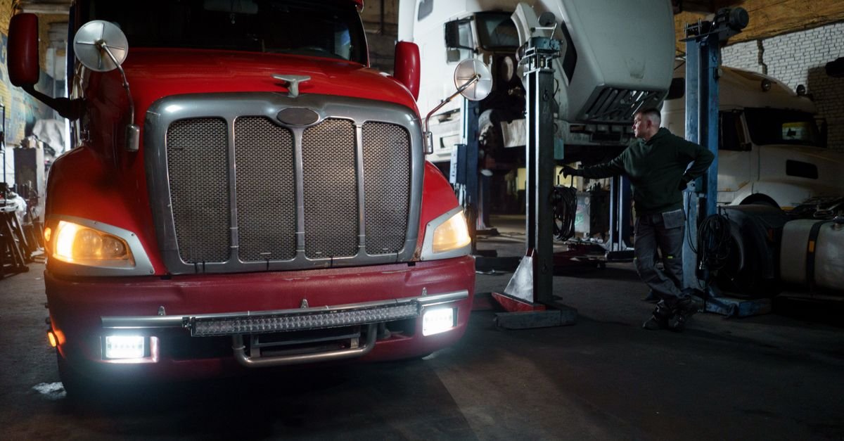 A red truck and raised vehicles inside a fleet maintenance garage with a mechanic at work