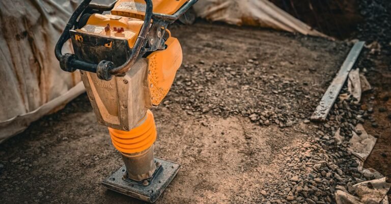Close-up of a vibratory plate compactor on a construction site with gravel and loose soil