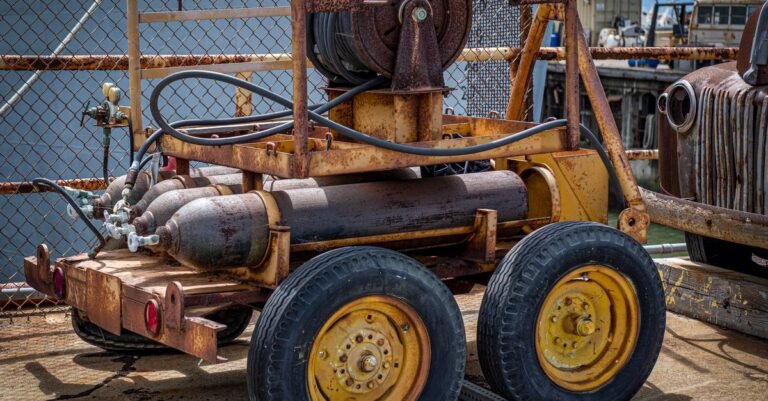 An old industrial cart loaded with hoses and tanks standing outside in the sun