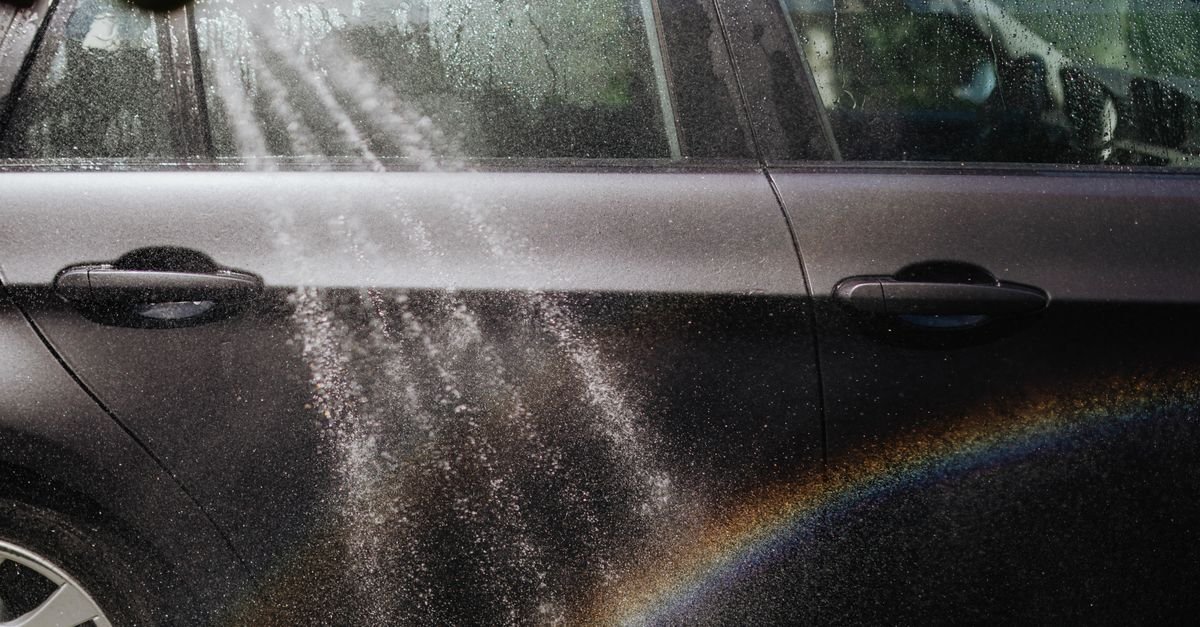 Close-up of a car being washed with a visible rainbow in sunlight