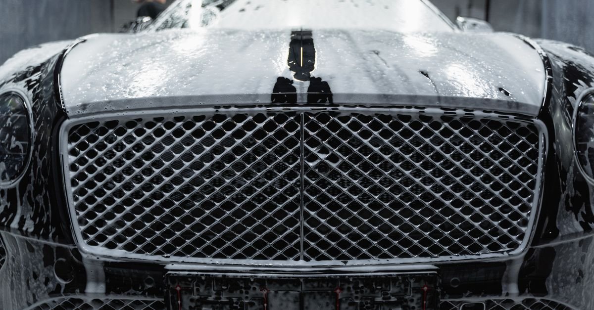 A close-up of a luxurious black car being cleaned with foamy soap at a carwash