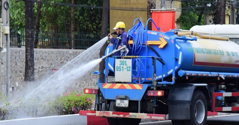 A worker running a long high-pressure line from a water truck along a city street