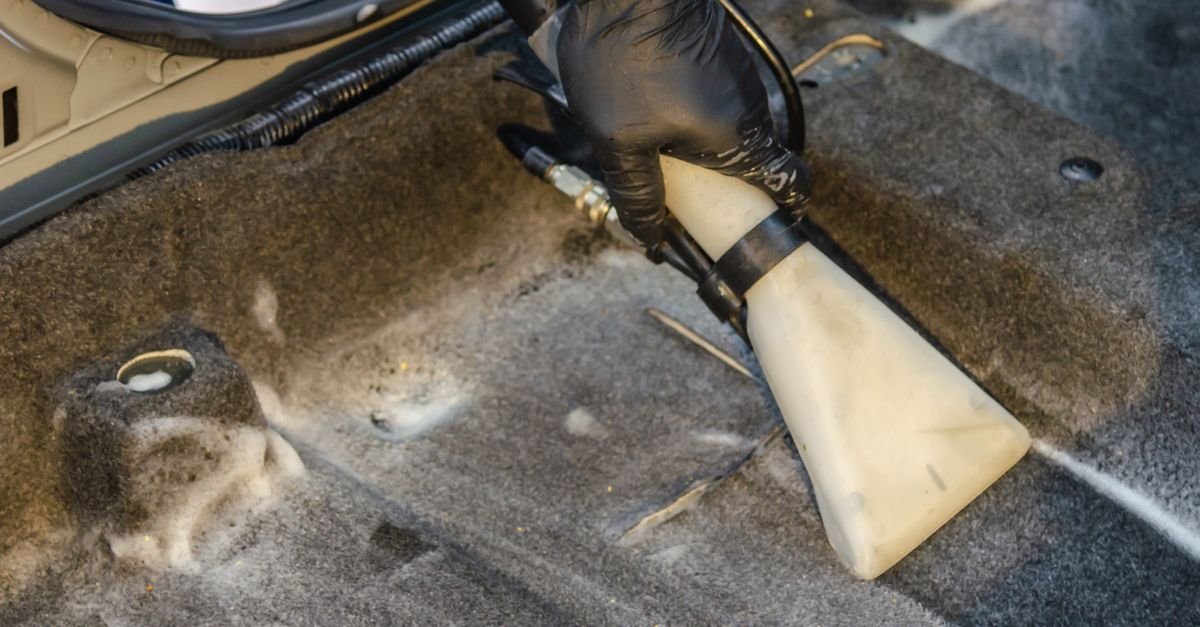 A gloved hand working an extraction tool across a car interior carpet, the job the heated extractor class is actually built for