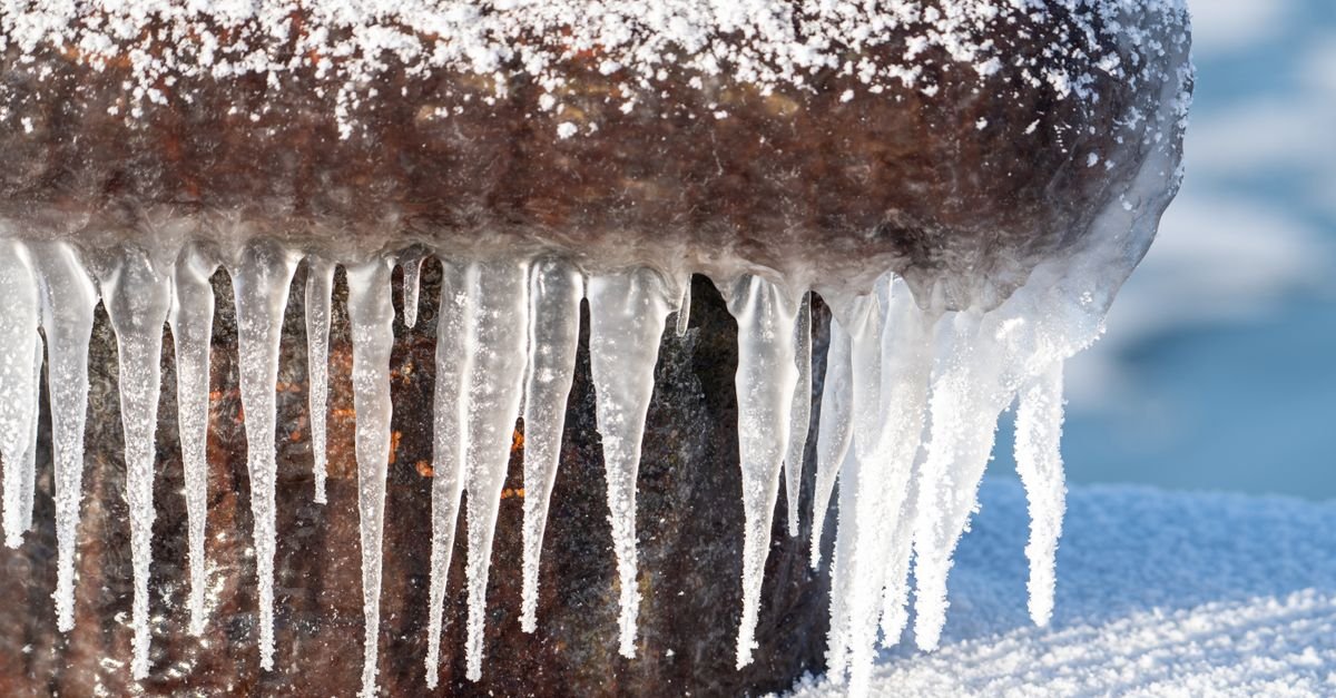 Clear icicles hanging from an iron bollard in a snowy harbour