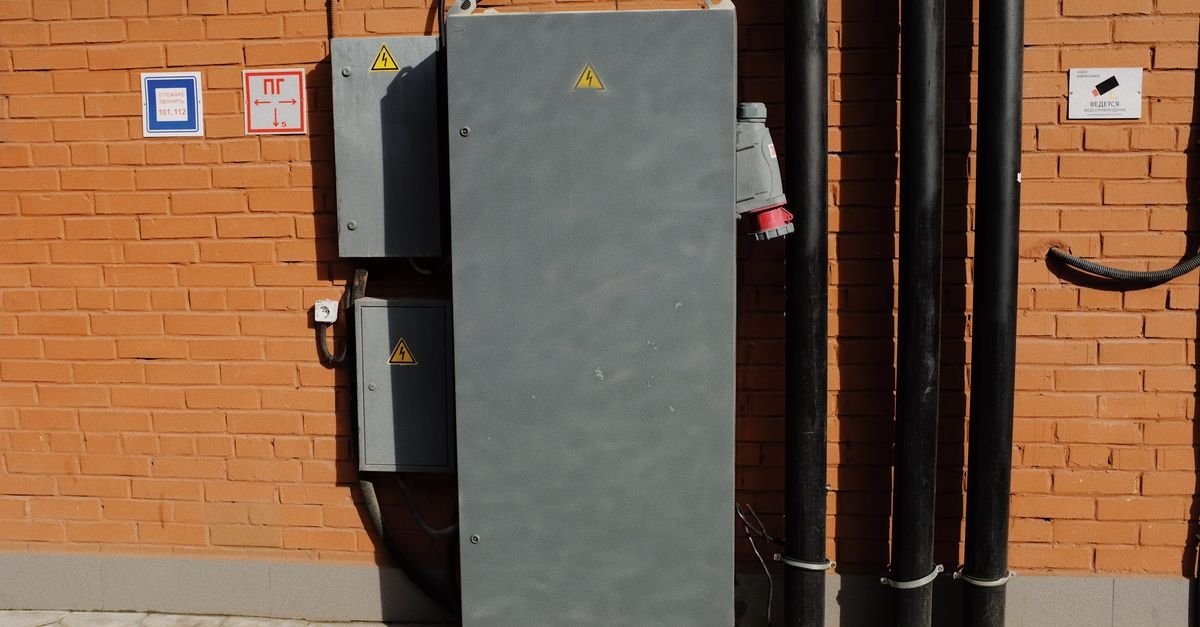 An outdoor electrical supply cabinet fixed to a brick wall in bright sunlight