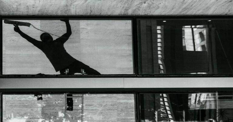 Silhouette of a window cleaner drawing a squeegee across a pane of building glass