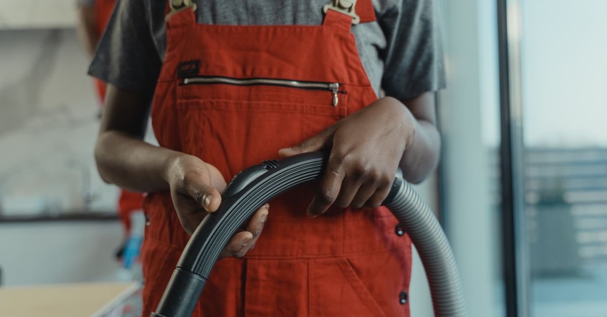 A gloved hand gripping the corrugated hose of a vacuum, showing the bore and the ribbed wall